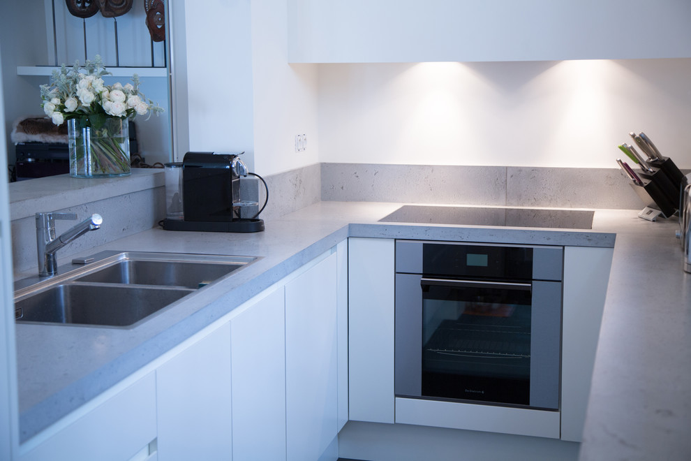 Expansive contemporary u-shaped enclosed kitchen in Angers with a double-bowl sink, flat-panel cabinets, white cabinets, concrete worktops, grey splashback and cement tile splashback.