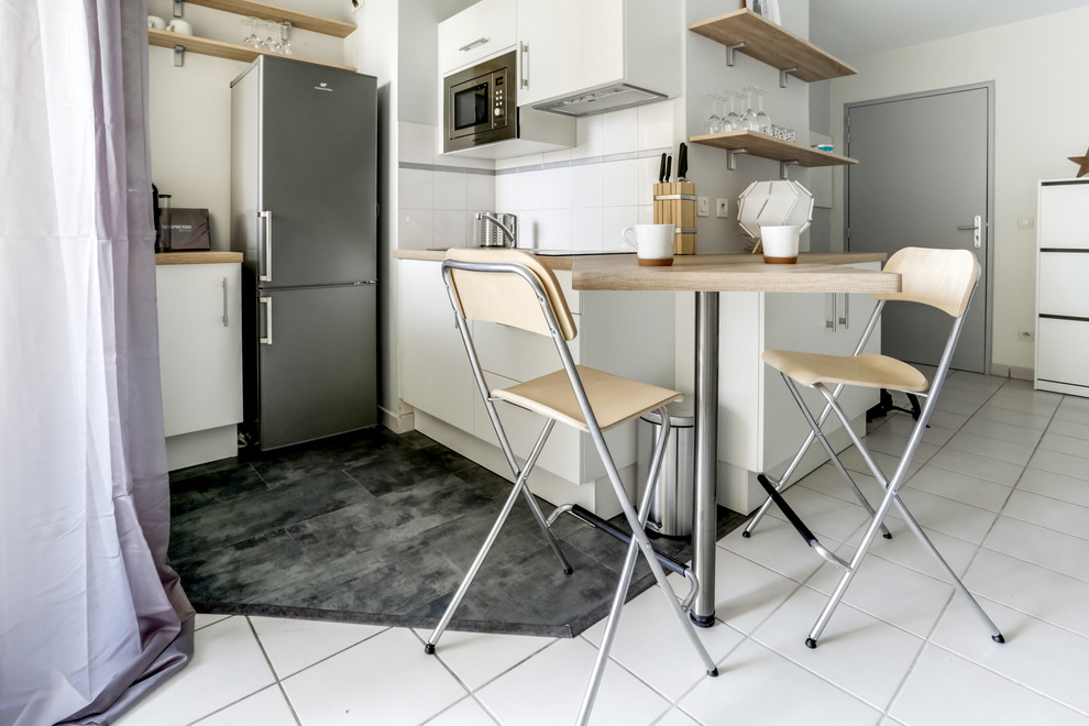 Inredning av ett minimalistiskt litet, avskilt kök, med luckor med profilerade fronter, vitt stänkskydd, rostfria vitvaror, skåp i rostfritt stål, träbänkskiva, glaspanel som stänkskydd, cementgolv, en köksö och svart golv