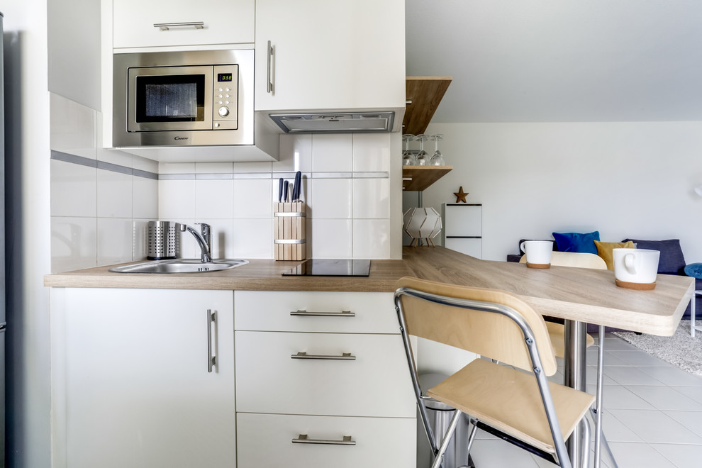 This is an example of a small scandinavian kitchen/diner in Bordeaux with a single-bowl sink, beaded cabinets, white cabinets, laminate countertops, white splashback, ceramic splashback, stainless steel appliances, lino flooring, a breakfast bar and grey floors.