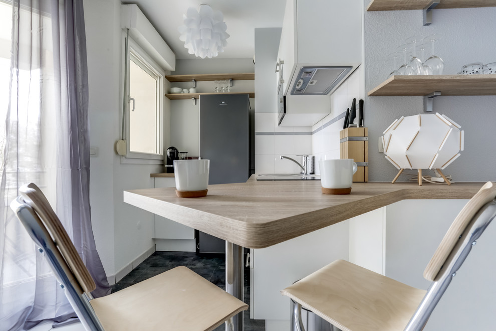 Foto på ett litet, avskilt minimalistiskt kök, med luckor med profilerade fronter, vitt stänkskydd, rostfria vitvaror, skåp i rostfritt stål, träbänkskiva, glaspanel som stänkskydd, cementgolv, en köksö och svart golv