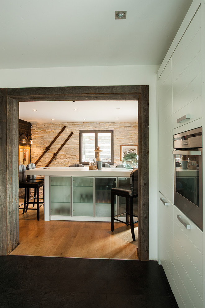 Idée de décoration pour une cuisine chalet de taille moyenne avec un placard à porte affleurante, des portes de placard blanches, un électroménager en acier inoxydable, un sol en carrelage de céramique et îlot.