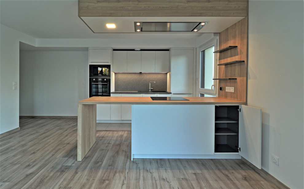 Photo of a medium sized contemporary u-shaped open plan kitchen in Other with a submerged sink, flat-panel cabinets, white cabinets, wood worktops, grey splashback, slate splashback, stainless steel appliances, laminate floors, an island, brown floors and brown worktops.