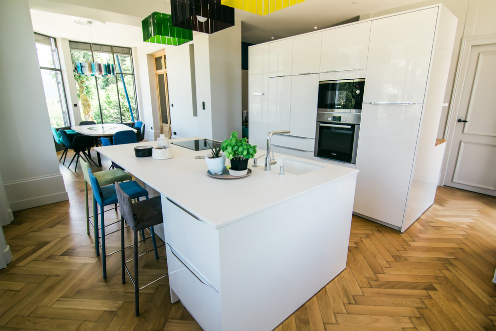 Ejemplo de cocina contemporánea abierta con fregadero integrado, suelo de madera clara y una isla