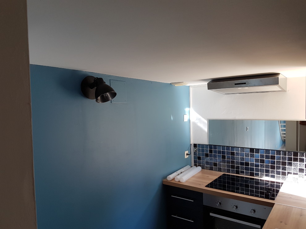 Bild på ett litet funkis kök, med en enkel diskho, svarta skåp, träbänkskiva, svart stänkskydd, stänkskydd i mosaik, svarta vitvaror, vinylgolv och grått golv