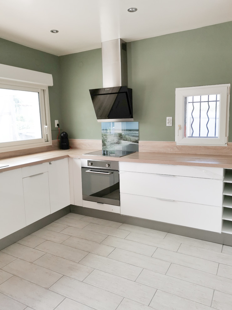 This is an example of a large rural l-shaped open plan kitchen in Bordeaux with a submerged sink, beaded cabinets, white cabinets, wood worktops, multi-coloured splashback, glass sheet splashback, black appliances, ceramic flooring, no island, white floors and beige worktops.