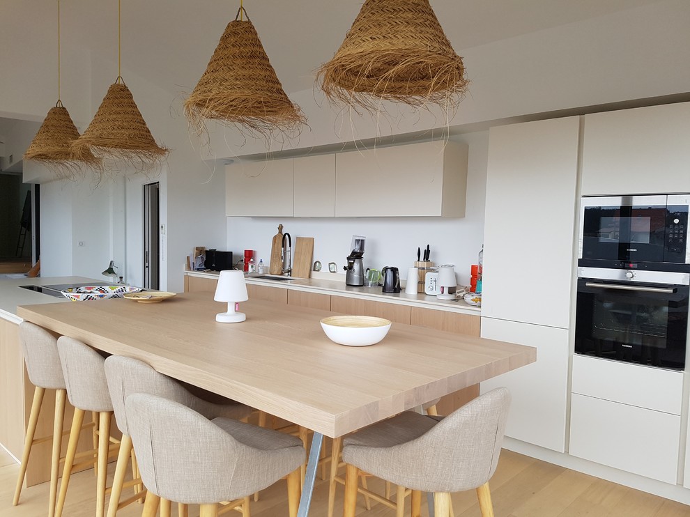 Photo of a large nautical galley kitchen/diner in Bordeaux with a submerged sink, beaded cabinets, beige cabinets, quartz worktops, light hardwood flooring, an island, white splashback, black appliances and beige floors.