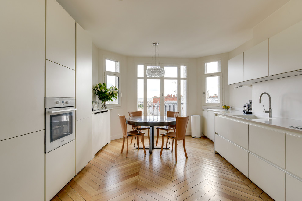 Design ideas for a large contemporary galley kitchen/diner in Paris with an integrated sink, white splashback, integrated appliances, light hardwood flooring, white worktops, flat-panel cabinets, no island, beige floors and white cabinets.