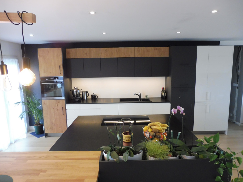 Foto på ett stort industriellt svart kök med öppen planlösning, med en dubbel diskho, granitbänkskiva, vitt stänkskydd, integrerade vitvaror och en köksö