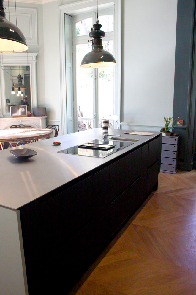 Exempel på ett stort modernt svart linjärt svart kök och matrum, med en undermonterad diskho, svart stänkskydd, stänkskydd i marmor, ljust trägolv, beiget golv, luckor med profilerade fronter, skåp i ljust trä, svarta vitvaror och en köksö
