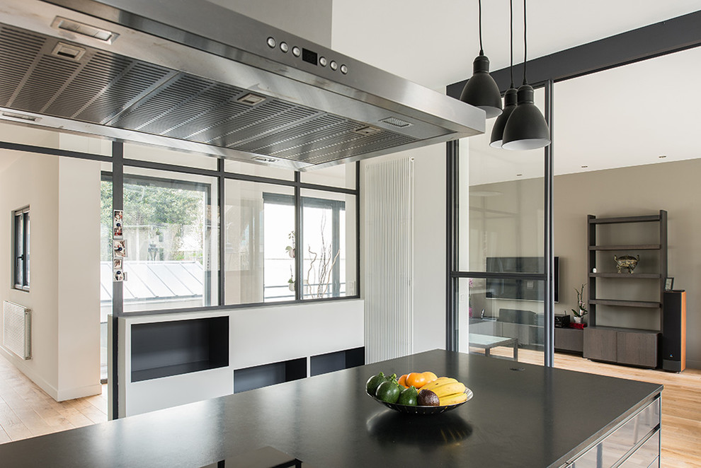 This is an example of a large contemporary open plan kitchen in Paris with an integrated sink, stainless steel cabinets, granite worktops, stainless steel appliances, ceramic flooring and an island.