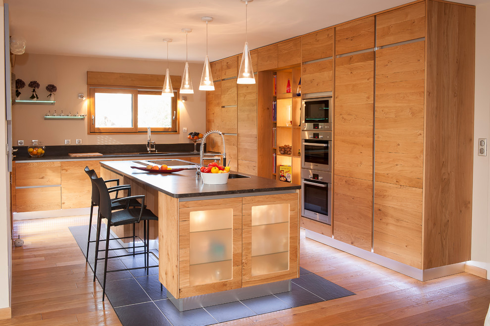 Cette image montre une grande cuisine américaine bicolore chalet en L et bois brun avec un placard à porte plane, un électroménager en acier inoxydable, un sol en bois brun et îlot.