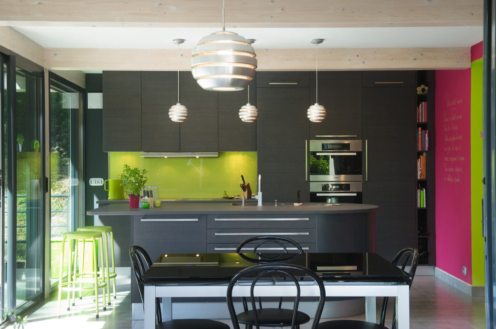 Bild på ett mellanstort funkis kök, med släta luckor, grå skåp, grönt stänkskydd, glaspanel som stänkskydd, rostfria vitvaror och en köksö