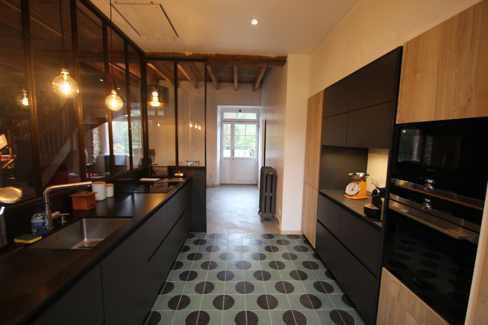 This is an example of a medium sized urban galley enclosed kitchen in Rennes with an integrated sink, flat-panel cabinets, black cabinets, granite worktops, black splashback, black appliances, cement flooring, turquoise floors and black worktops.