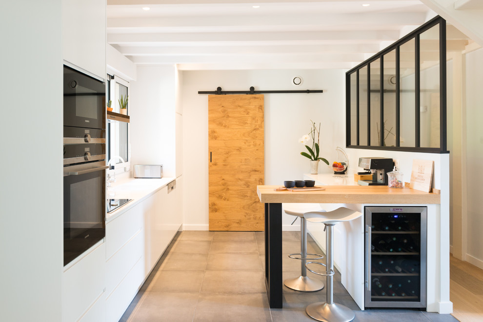 Large scandi kitchen in Bordeaux with white cabinets, quartz worktops, ceramic flooring, grey floors, white worktops, flat-panel cabinets, black appliances and a breakfast bar.