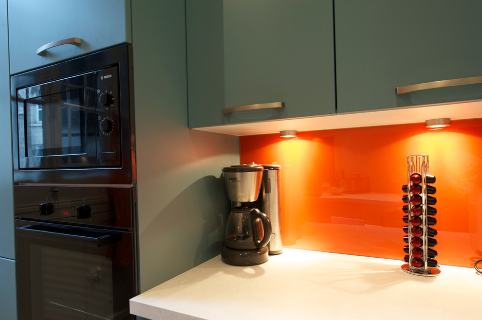 На фото: большая отдельная, прямая кухня в стиле модернизм с одинарной мойкой, плоскими фасадами, синими фасадами, столешницей из ламината, оранжевым фартуком, фартуком из стекла, черной техникой, полом из керамической плитки и полуостровом с