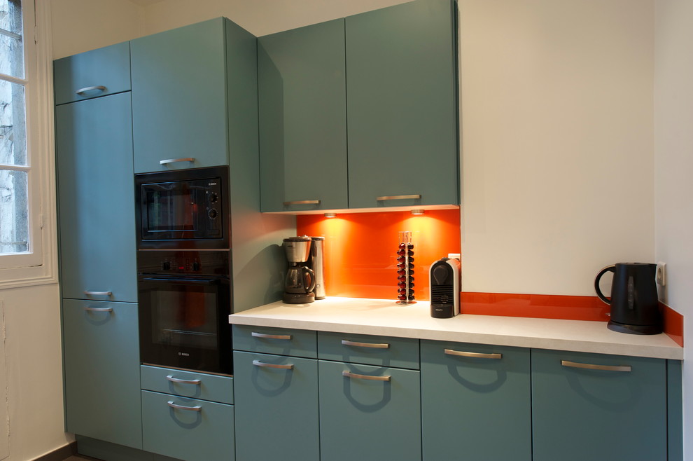 パリにあるお手頃価格の広いコンテンポラリースタイルのおしゃれなキッチン (シングルシンク、フラットパネル扉のキャビネット、青いキャビネット、ラミネートカウンター、オレンジのキッチンパネル、ガラス板のキッチンパネル、黒い調理設備、セラミックタイルの床) の写真