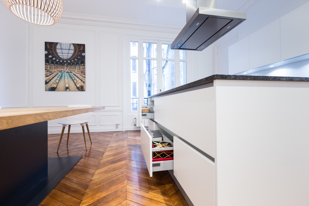 Esempio di una grande cucina design con lavello sottopiano, ante bianche, top in granito, elettrodomestici neri e pavimento in legno massello medio