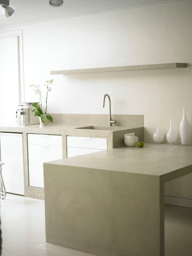 Modern inredning av ett mellanstort kök, med vita skåp, bänkskiva i betong och en halv köksö