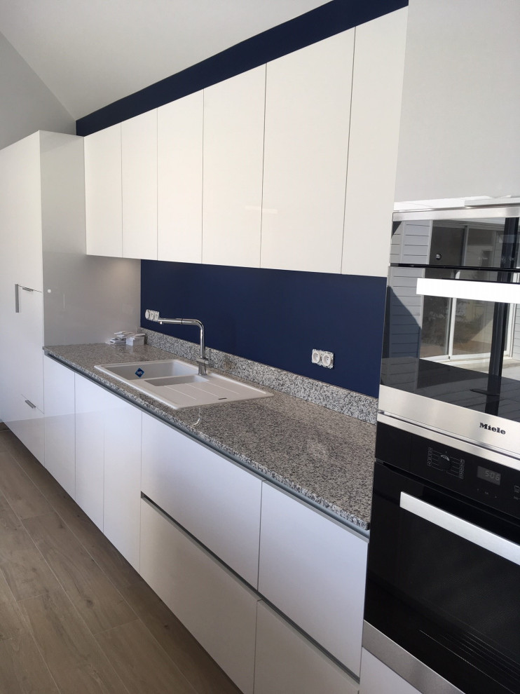 Photo of a medium sized contemporary galley enclosed kitchen in Other with a submerged sink, beaded cabinets, white cabinets, granite worktops, grey splashback, stainless steel appliances, light hardwood flooring, an island and grey worktops.