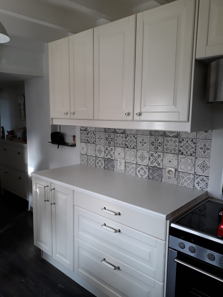 Bild på ett avskilt, litet lantligt vit linjärt vitt kök, med en integrerad diskho, luckor med profilerade fronter, vita skåp, laminatbänkskiva, grått stänkskydd, stänkskydd i keramik, rostfria vitvaror, laminatgolv och svart golv
