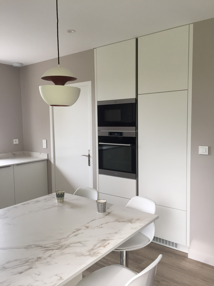 Design ideas for a large modern u-shaped open plan kitchen in Toulouse with an integrated sink, beaded cabinets, white cabinets, quartz worktops, white splashback, glass tiled splashback, stainless steel appliances, light hardwood flooring, white worktops, an island and grey floors.