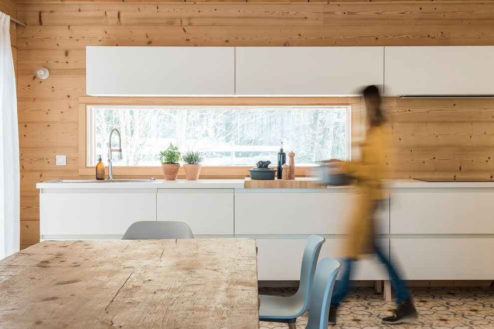 Photo of a medium sized modern single-wall kitchen/diner in Lyon with a double-bowl sink, flat-panel cabinets, white cabinets, beige splashback, wood splashback, ceramic flooring and multi-coloured floors.