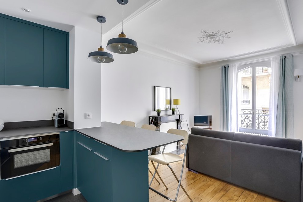 Small contemporary u-shaped open plan kitchen in Paris with blue cabinets, laminate countertops, a single-bowl sink, flat-panel cabinets, black splashback, stainless steel appliances, ceramic flooring, an island, grey floors and black worktops.