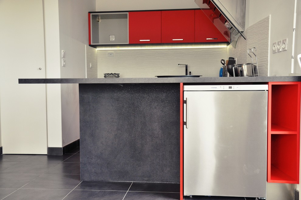 Foto på ett litet funkis kök, med en undermonterad diskho, röda skåp, svart stänkskydd, rostfria vitvaror och klinkergolv i porslin