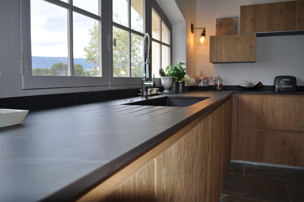 Esempio di una grande cucina design con lavello integrato, ante a filo, ante in legno scuro, top in superficie solida, paraspruzzi nero, elettrodomestici neri, pavimento in travertino, pavimento beige e top nero