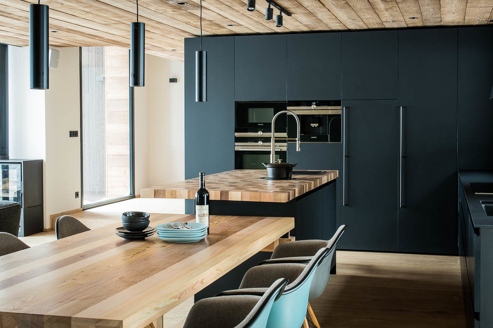 Foto di una cucina minimal di medie dimensioni con lavello da incasso, ante lisce, ante beige, top in legno, paraspruzzi nero, elettrodomestici neri, parquet chiaro e pavimento beige