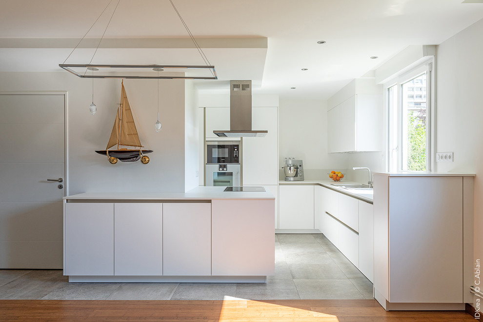 Diseño de cocina actual de tamaño medio abierta con armarios con rebordes decorativos, puertas de armario blancas, salpicadero blanco, electrodomésticos con paneles, suelo de baldosas de cerámica, península, suelo gris y encimeras blancas