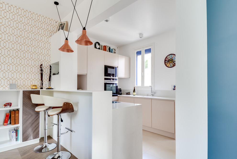 This is an example of a small contemporary u-shaped kitchen/diner in Paris with flat-panel cabinets, beige cabinets, black appliances, a breakfast bar, a submerged sink and grey splashback.
