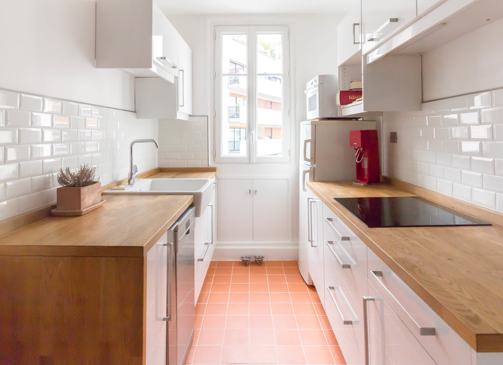 パリにあるお手頃価格の小さなコンテンポラリースタイルのおしゃれなキッチン (一体型シンク、フラットパネル扉のキャビネット、白いキャビネット、木材カウンター、白いキッチンパネル、サブウェイタイルのキッチンパネル、パネルと同色の調理設備、テラコッタタイルの床、アイランドなし、赤い床、茶色いキッチンカウンター) の写真
