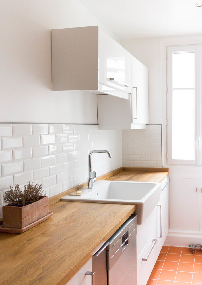 This is an example of a small contemporary galley enclosed kitchen in Paris with an integrated sink, flat-panel cabinets, white cabinets, wood worktops, white splashback, metro tiled splashback, integrated appliances, terracotta flooring, no island, red floors and brown worktops.