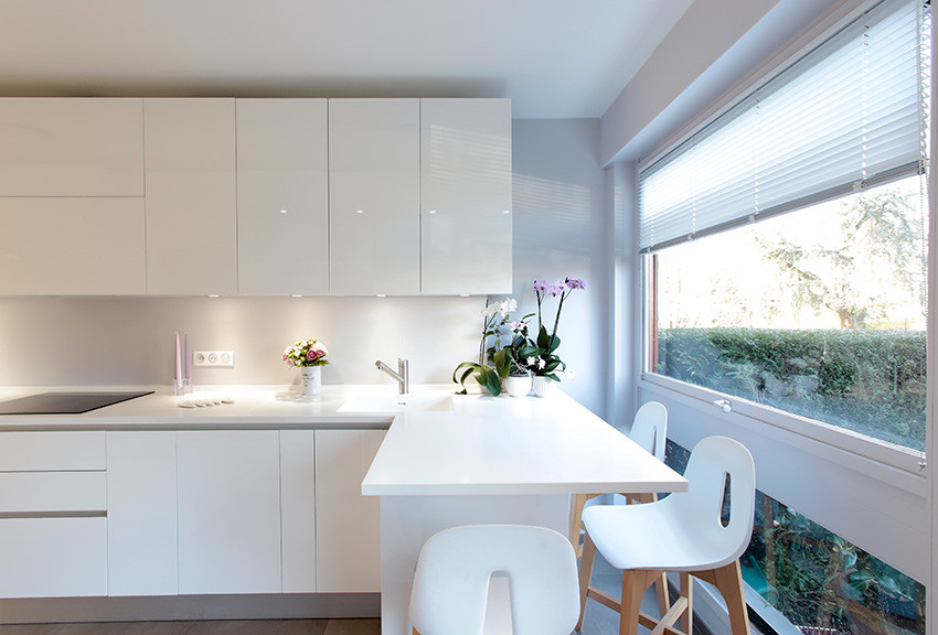 Photo of a small contemporary galley enclosed kitchen in Paris with a submerged sink, flat-panel cabinets, white cabinets, composite countertops, white splashback, black appliances, ceramic flooring, grey floors and white worktops.
