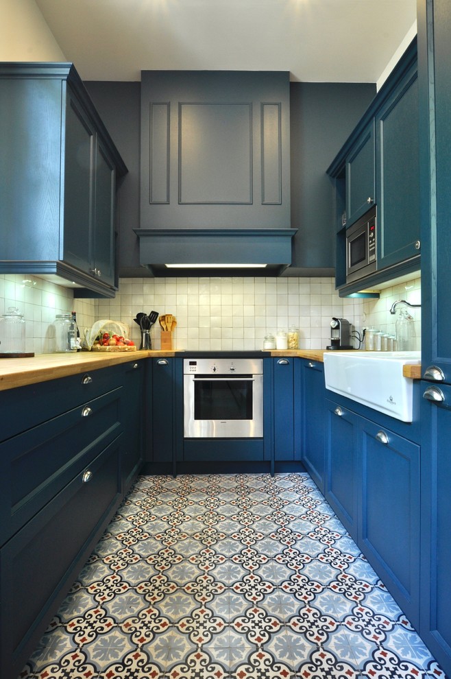 Photo of a small traditional u-shaped enclosed kitchen in Paris with an integrated sink, shaker cabinets, blue cabinets, wood worktops, white splashback, ceramic splashback, stainless steel appliances and cement flooring.