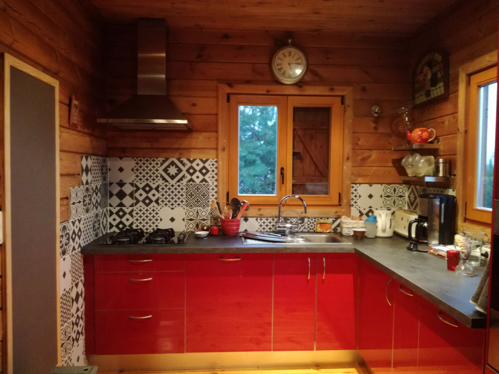 Пример оригинального дизайна: угловая кухня-гостиная среднего размера в классическом стиле с красными фасадами, столешницей из ламината, серым фартуком, фартуком из цементной плитки, черной техникой и серой столешницей