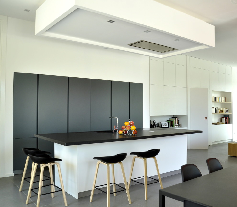 Стильный дизайн: параллельная кухня-гостиная среднего размера в современном стиле с монолитной мойкой, техникой под мебельный фасад, островом, черно-белыми фасадами и барной стойкой - последний тренд