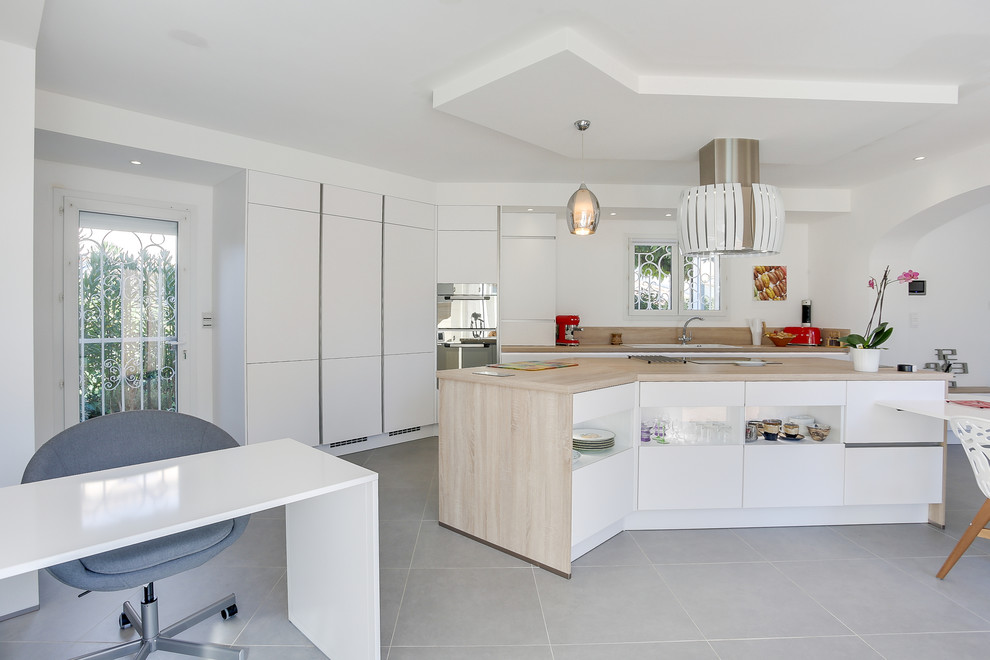 Example of a large trendy galley gray floor open concept kitchen design in Marseille with a drop-in sink, flat-panel cabinets, white cabinets, wood countertops, beige backsplash, wood backsplash, black appliances, an island and beige countertops