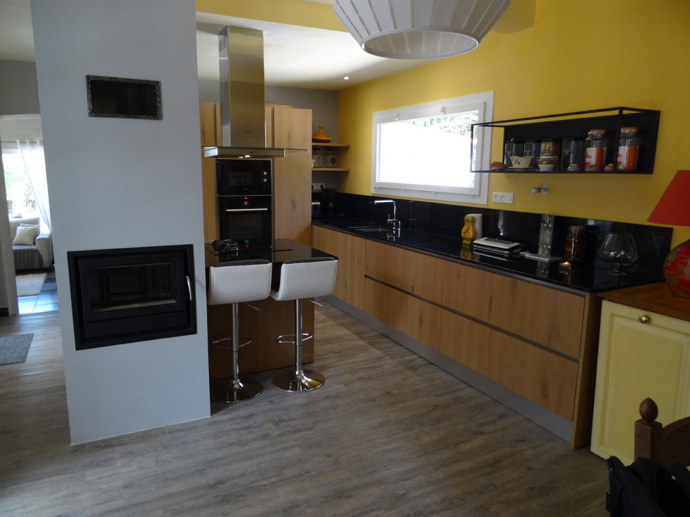 Photo of a large urban l-shaped open plan kitchen in Marseille with an integrated sink, beaded cabinets, light wood cabinets, granite worktops, black splashback, black appliances, medium hardwood flooring, an island and grey floors.