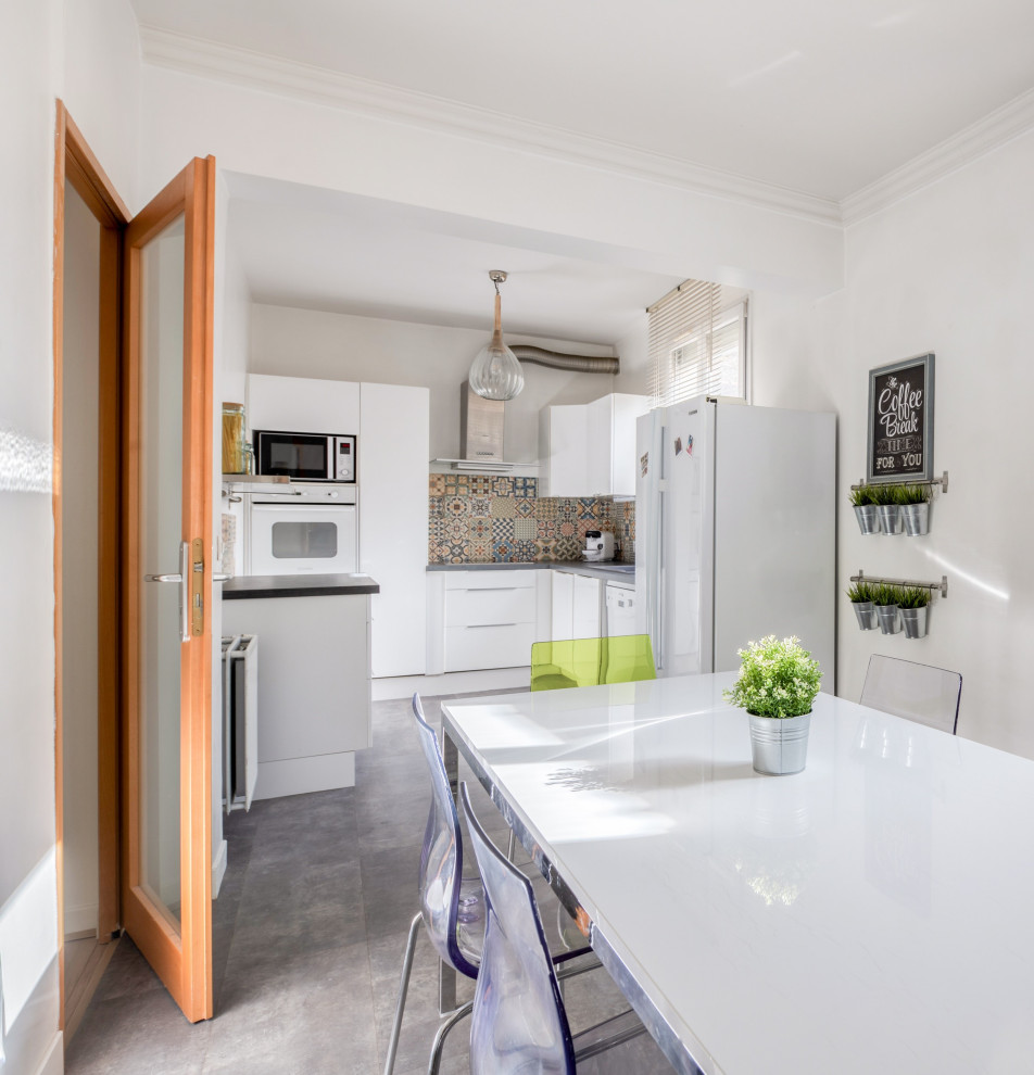 Foto på ett funkis grå kök, med vita skåp, flerfärgad stänkskydd, stänkskydd i cementkakel, vita vitvaror, klinkergolv i porslin, en köksö och grått golv