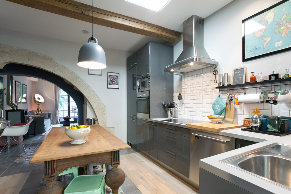 Large bohemian l-shaped kitchen/diner in Montpellier with grey cabinets, white splashback, metro tiled splashback, stainless steel appliances, light hardwood flooring, no island and a submerged sink.