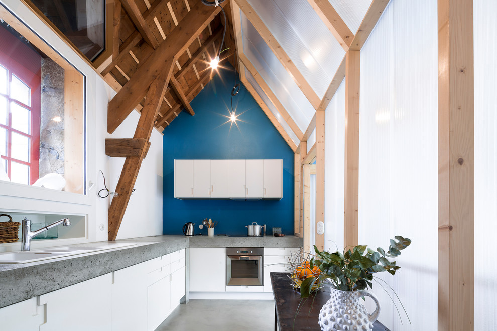 Пример оригинального дизайна: угловая кухня среднего размера в современном стиле с накладной мойкой, плоскими фасадами, белыми фасадами, техникой из нержавеющей стали, бетонным полом, обеденным столом, столешницей из бетона и синим фартуком без острова