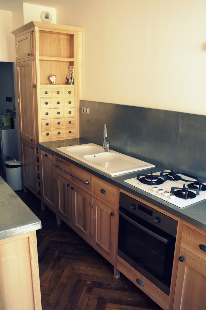 Bild på ett avskilt, mellanstort industriellt grå linjärt grått kök, med en undermonterad diskho, luckor med profilerade fronter, skåp i ljust trä, bänkskiva i rostfritt stål, grått stänkskydd, rostfria vitvaror, mellanmörkt trägolv och brunt golv