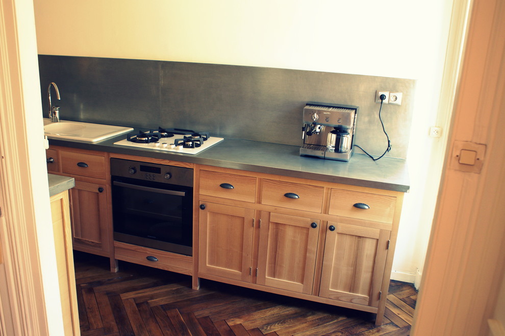 Foto på ett avskilt, mellanstort industriellt grå linjärt kök, med en undermonterad diskho, luckor med profilerade fronter, skåp i ljust trä, bänkskiva i rostfritt stål, grått stänkskydd och rostfria vitvaror