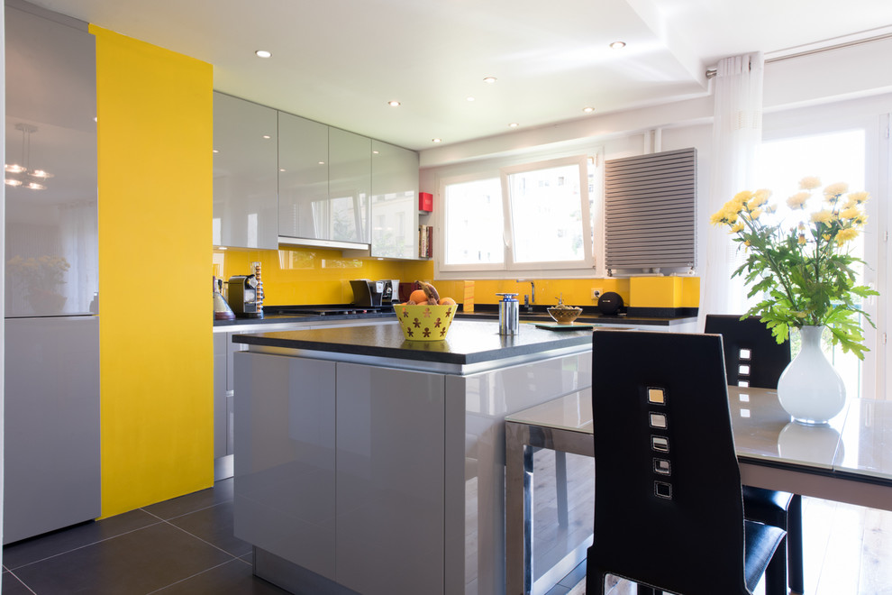 This is an example of a medium sized bohemian u-shaped kitchen/diner in Paris with an integrated sink, beaded cabinets, grey cabinets, granite worktops, yellow splashback, glass tiled splashback, stainless steel appliances and an island.