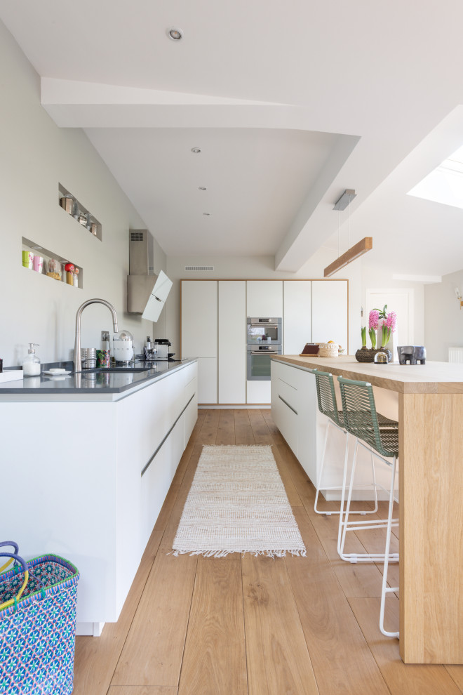 Photo of a large scandi l-shaped kitchen in Paris with a submerged sink, flat-panel cabinets, white cabinets, stainless steel worktops, integrated appliances, medium hardwood flooring, an island, beige floors and grey worktops.