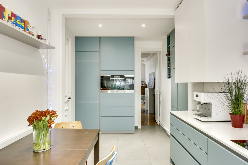 Idée de décoration pour une cuisine parallèle et encastrable design fermée et de taille moyenne avec une crédence bleue, carreaux de ciment au sol et un sol beige.