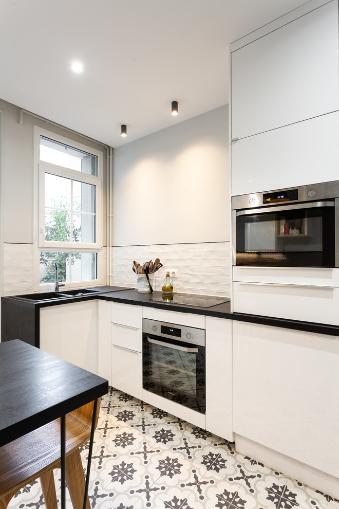 Design ideas for a medium sized contemporary galley enclosed kitchen in Paris with a double-bowl sink, beaded cabinets, white cabinets, laminate countertops, white splashback, terracotta splashback, stainless steel appliances, cement flooring, no island, grey floors and black worktops.