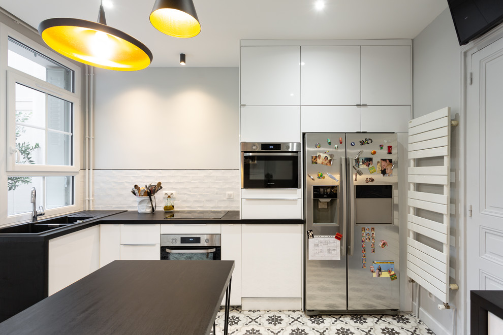 Photo of a medium sized contemporary galley enclosed kitchen in Paris with a double-bowl sink, beaded cabinets, white cabinets, laminate countertops, white splashback, terracotta splashback, stainless steel appliances, cement flooring, no island, grey floors and black worktops.